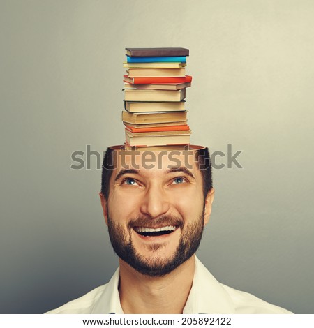 smiley young man looking up at books in the head over grey background