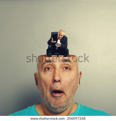 amazed senior man with open head. angry small businessman screaming with megaphone in the man\'s head. photo over grey background