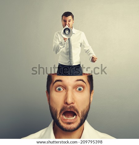 stressed young man with angry screaming man in his head over grey background