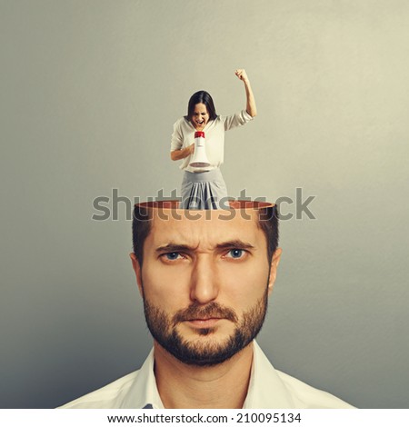 young man with open head. small angry woman standing in the man\'s head and screaming with megaphone. photo over grey background