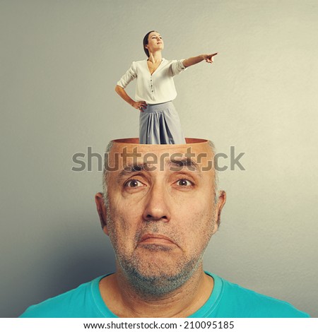 depressed senior man with open head. young smiley woman standing in the head and pointing at something. photo over grey background