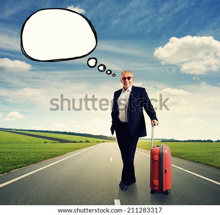 smiley senior businessman in formal wear and sunglasses with suitcase standing on the road. concept photo with drawing empty speech balloon at outdoor