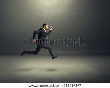happy businessman in formal wear running over dark background