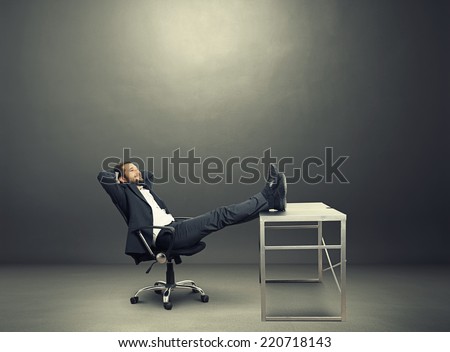 young businessman put his feet up on the table, resting and smiling. photo in the dark room