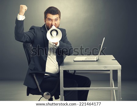 aggressive businessman screaming with megaphone and looking at camera. photo in the dark room