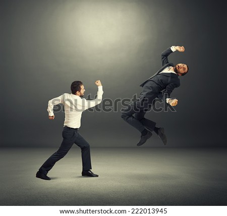 two businessmen in fight. one man standing and hitting, second man flying and screaming. photo in the dark room