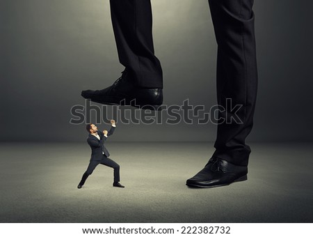 concept photo of conflict between subordinate and boss. angry young businessman showing fist and looking up at big boss. photo in the dark room