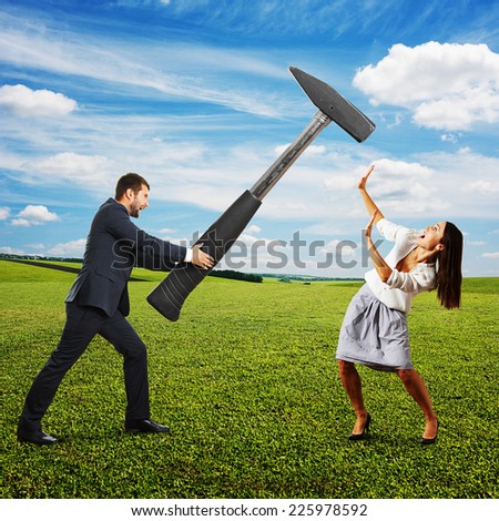 angry screaming man holding big hammer and hitting scared woman. photo at outdoor