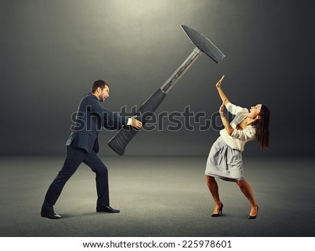 angry screaming man holding big hammer and hitting scared woman. photo in the dark room