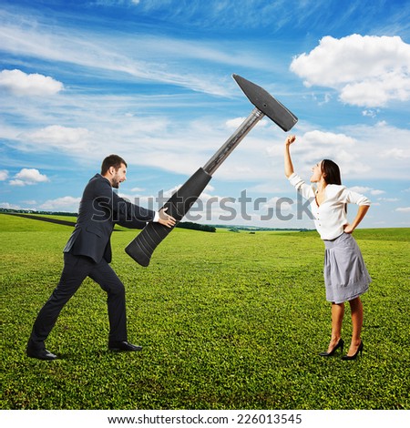 concept photo of conflict between man and woman. angry screaming man holding big hammer and hitting, woman showing fist and shouting. photo at outdoor