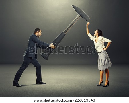 concept photo of conflict between man and woman. angry screaming man holding big hammer and hitting, woman showing fist and shouting. photo over dark background