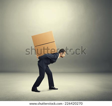 tired young businessman carrying on the back two heavy boxes. photo in the grey room