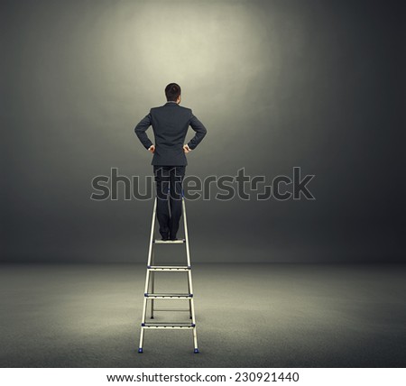 back view of businessman standing on the pair of steps and looking forward. photo in the dark room