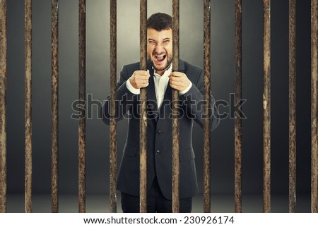 angry screaming businessman behind the prison cell over dark background