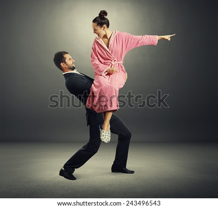 angry screaming woman in dressing gown sitting on the hands her husband over dark background