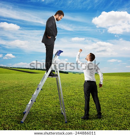 angry screaming man looking at man on the stepladder and showing his fist. photo at outdoor