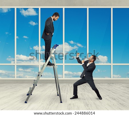 displeased businessman looking down at man in fighting stance. photo in room with big window