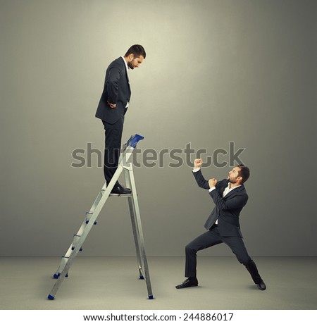 displeased businessman on the stepladder looking down at man in fighting stance. photo in the grey studio