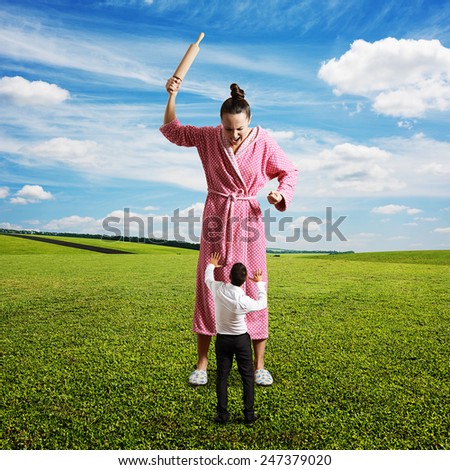 displeased housewife with rolling pin yelling at small startled husband. photo at outdoor