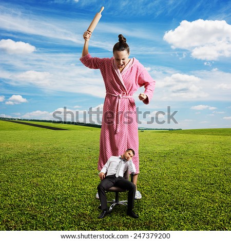 dissatisfied woman with rolling pin screaming at small lazy man on the chair. photo at outdoor