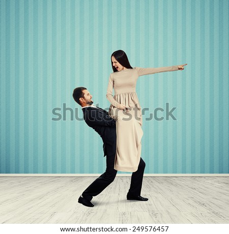 angry screaming woman looking at her man and pointing at something. photo in room with blue wall
