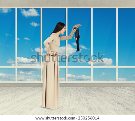 aggressive woman holding small man and yelling. photo in room with big windows