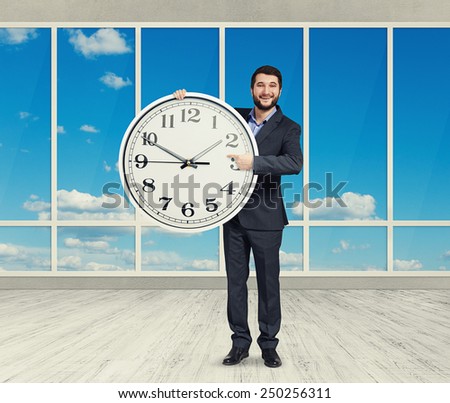 excited smiley businessman with big white clock standing in empty room with big windows