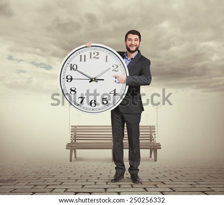 smiley businessman holding big clock, pointing at dial plate and looking at camera. photo at outdoor