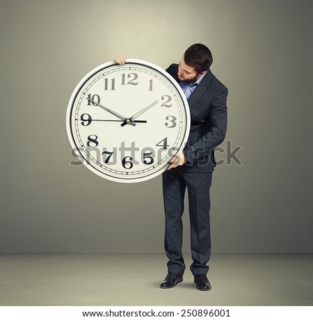 businessman holding big white clock and looking at clock dial over grey background