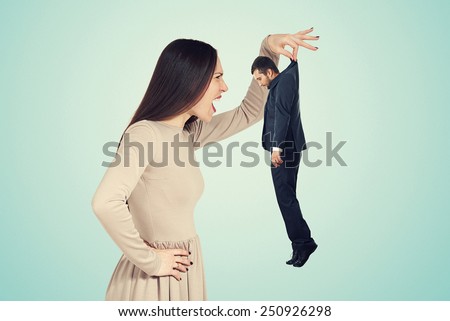 aggressive young woman holding small man and screaming at him. photo over blue background