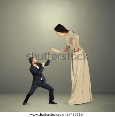 angry yelling woman showing fist to small scared man. photo over dark background