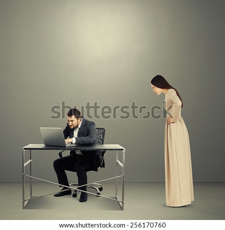 concentrated man looking at laptop, angry woman staring at man. photo in dark room