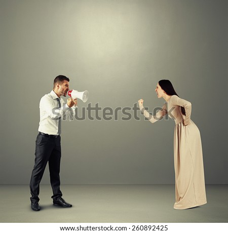 angry yelling woman showing fist to emotional man with megaphone. photo over dark background