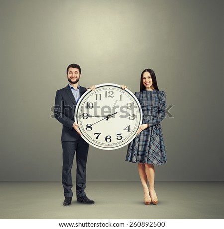 smiley couple with big white clock over grey background