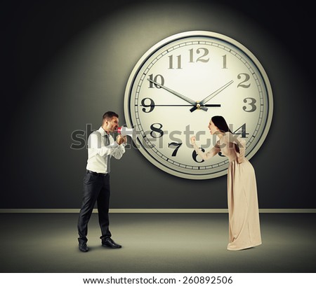 angry yelling woman and screaming man with megaphone in dark room with big clock on the wall