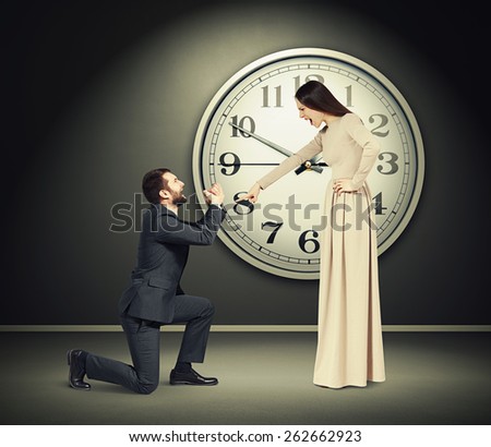 angry yelling woman pointing finger at crying man in dark room with big clock on the wall