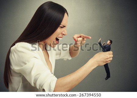 emotional woman holding in hand small scared man, pointing at him and yelling. photo over dark background
