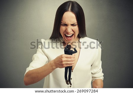 emotional woman holding in fist small scared man and yelling at him. photo on dark background