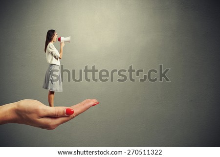 palm holding small screaming woman with megaphone over grey background. empty copyspace at right side