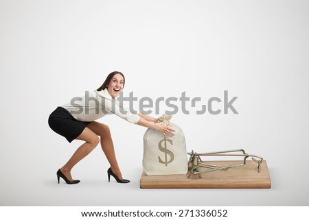 excited woman in formal wear reaching her arms to take bag with money in big mousetrap over light grey background