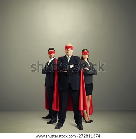 full length portrait of three superheroes in formal wear and red mask with cloak over light grey background