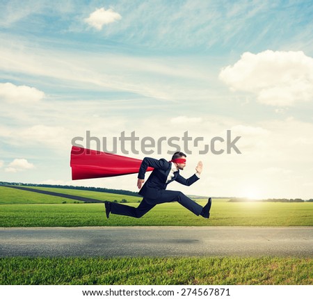 serious businessman wearing like superhero very fast running on the road over green fields and blue sky