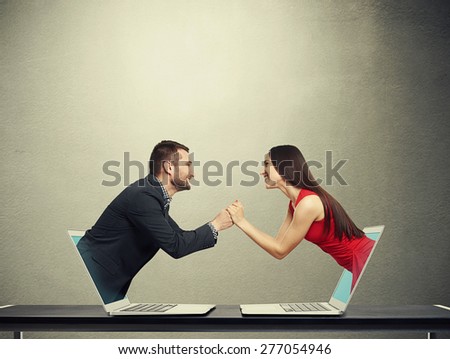 concept of love in social network. young man got out of the computer and holding hand of beautiful young woman who got out of another computer over dark background