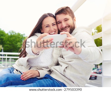 outdoor photo of smiley young couple sitting and taking a selfie