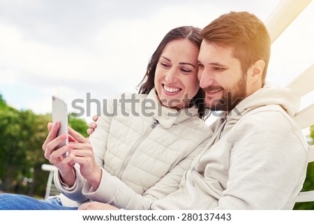 urban photo of young adult couple looking at cellphone and smiling