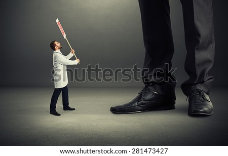 small screaming doctor holding placard and looking up at big legs over dark grey background