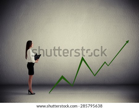 smiley businesswoman holding folder and looking at green diagram in dark grey room