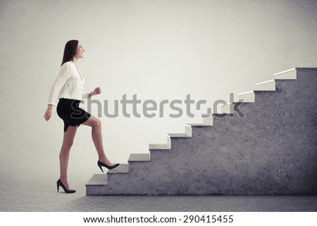 smiley businesswoman in formal wear walking up stairs over light grey background