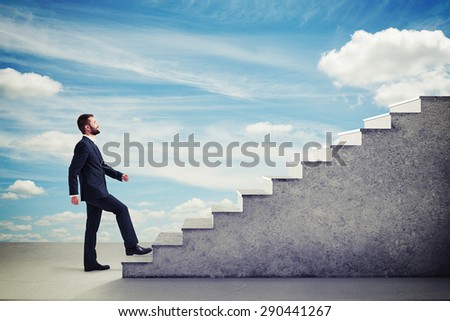 smiley businessman in formal wear walking up stairs over blue sky