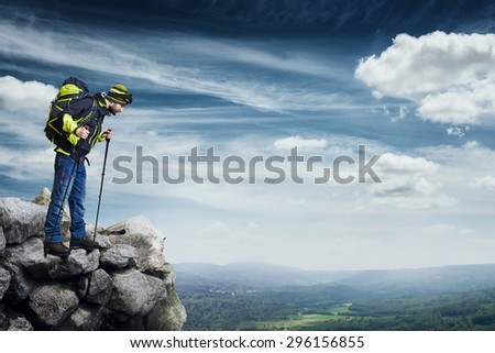 hiker with backpack and hiking poles standing on the top of rock and looking down